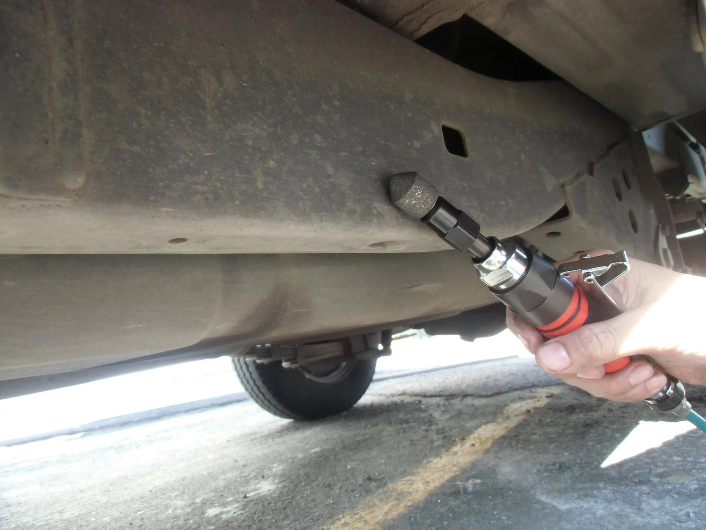 a person holding a wrench under a vehicle